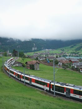 A train travels through the picturesque Lungern village in Switzerland, surrounded by lush green hills and misty mountains.